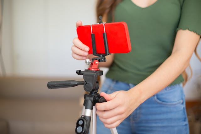 Close-up of hands setting up a smartphone on a red tripod mount for video recording