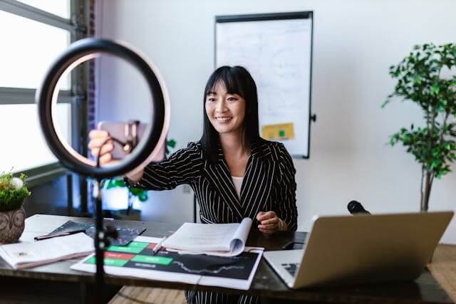 Woman filming a social media video with a ring light and digital tools at her desk
