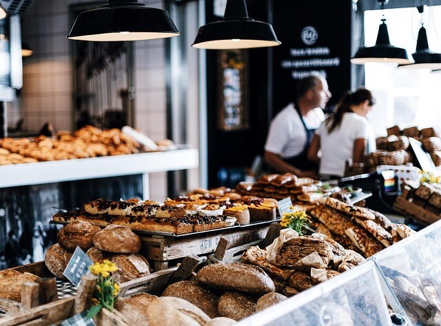 Interior of a bakery with loaves of bread and pastries on display, staff serving customers in the background