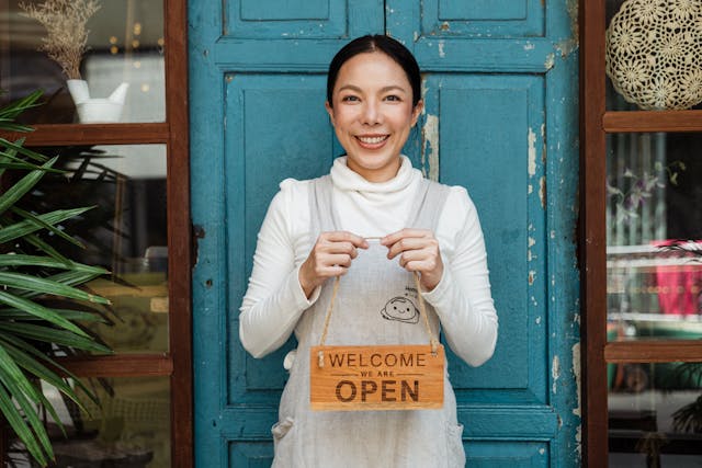 Smiling small business owner holding an open sign outside her shop