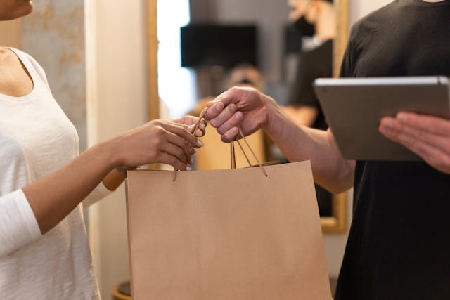 Store employee handing a shopping bag to a customer, symbolizing service that goes beyond sales.
