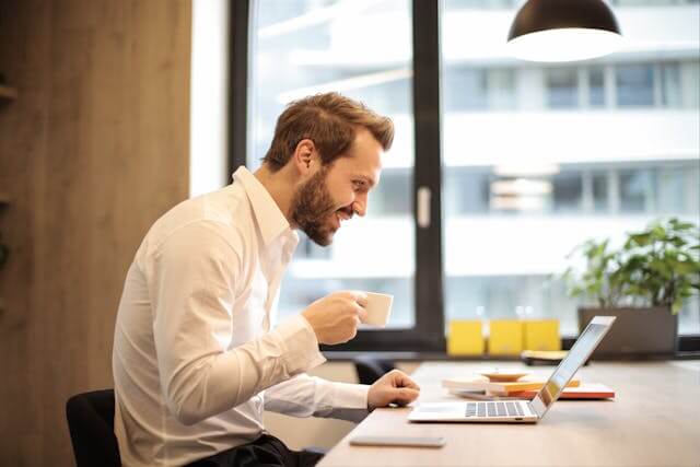 Business owner smiling while reading positive online customer reviews on a laptop.